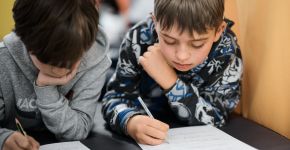Zwei Schüler arbeiten konzentriert und schreiben mit einem Stift auf Blätter.