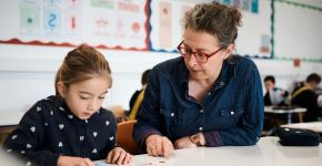 Eine Lehrerin übt mit einem Mädchen, beide schauen konzentriert in ein Heft.