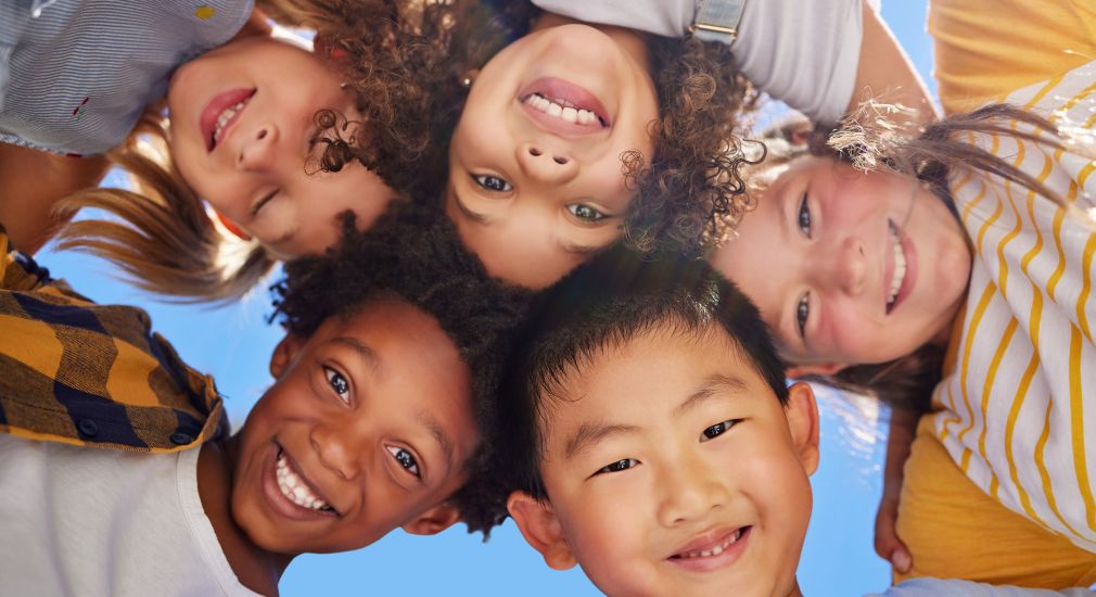 Fünf Kinder schauen von oben in eine Kamera, im Hintergrund ist ein blauer Himmel zu sehen.